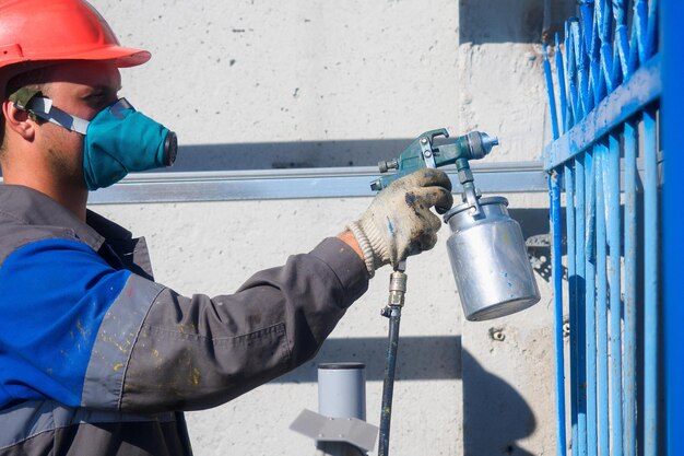 industrial-painter-respirator-helmet-paints-metal-fence-from-spray-gun-painting-fence-summer-day-authentic-workflow-professional-worker-overalls_230115-3899