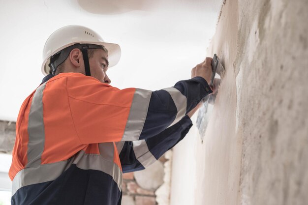 man-helmet-work-uniform-aligns-walls-ceiling-with-spatula-putty_363522-29