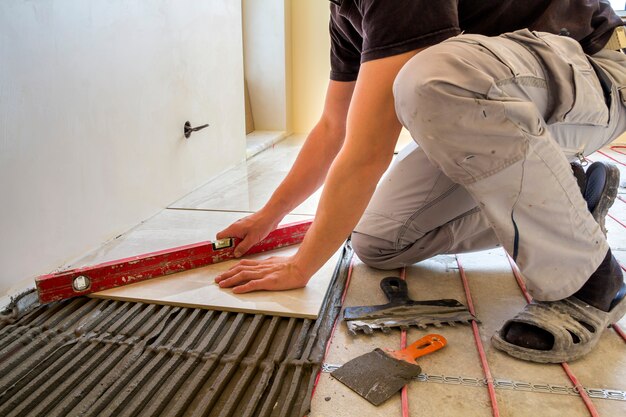 young-worker-tiler-installing-ceramic-tiles-using-lever-cement-floor-with-heating-red-electrical-cable-wire-system_127089-496